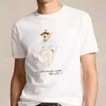 Ce T-shirt Ralph Lauren arbore un imprimé de l’élégante mascotte « Polo Bear » en salopette et casquette.