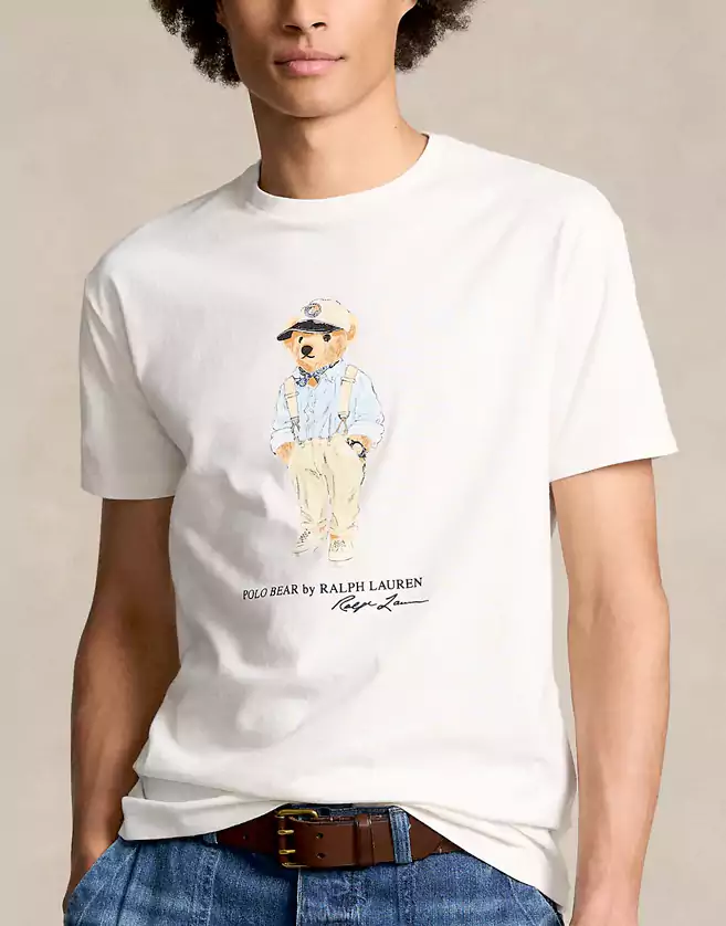 Ce T-shirt Ralph Lauren arbore un imprimé de l’élégante mascotte « Polo Bear » en salopette et casquette.